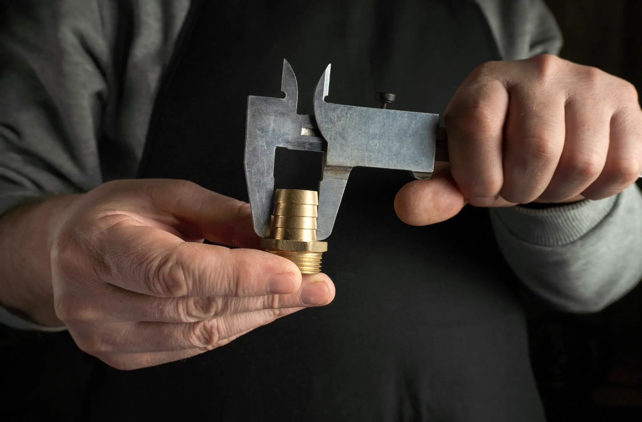 A machinist checking a brass fitting with a precision caliper